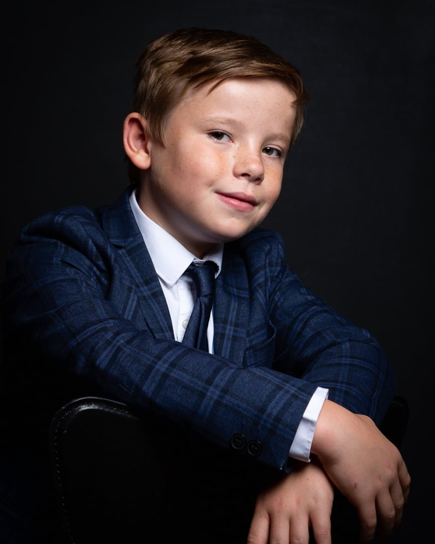 a young man poses in a suit and tie for a professional photo shoot