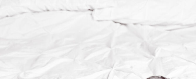 a black and white image of a newborn sleeping on their side on a white bed