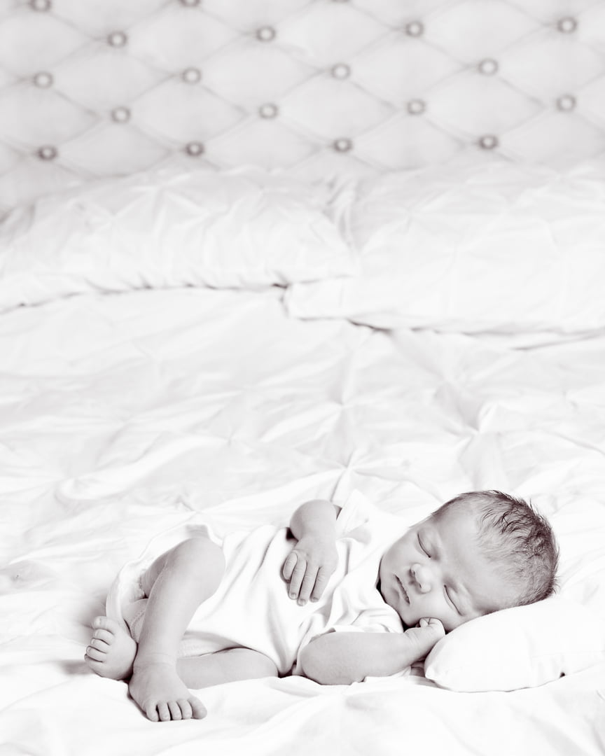 a black and white image of a newborn sleeping on their side on a white bed