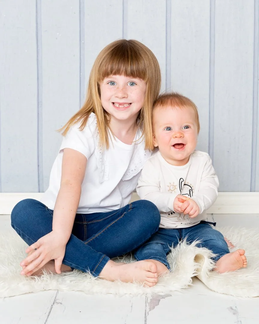 a brother and sister pose together in jeans and matching shirts.