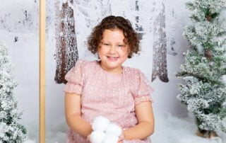 a little girl holds a pile of snowballs in a snow christmas photo shoot set