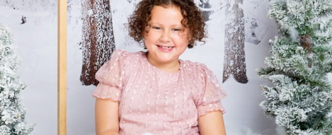 a little girl holds a pile of snowballs in a snow christmas photo shoot set