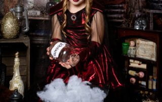 a girl dressed in a gothic style costume looks down at a crystal ball in a halloween themed photo shoot