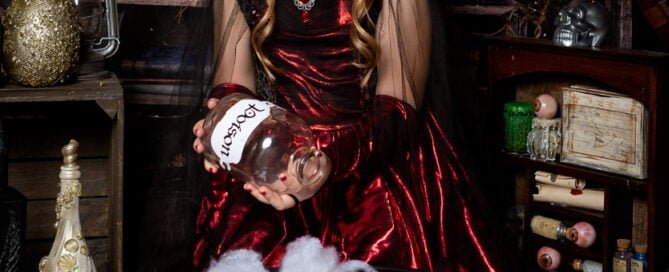 a girl dressed in a gothic style costume looks down at a crystal ball in a halloween themed photo shoot