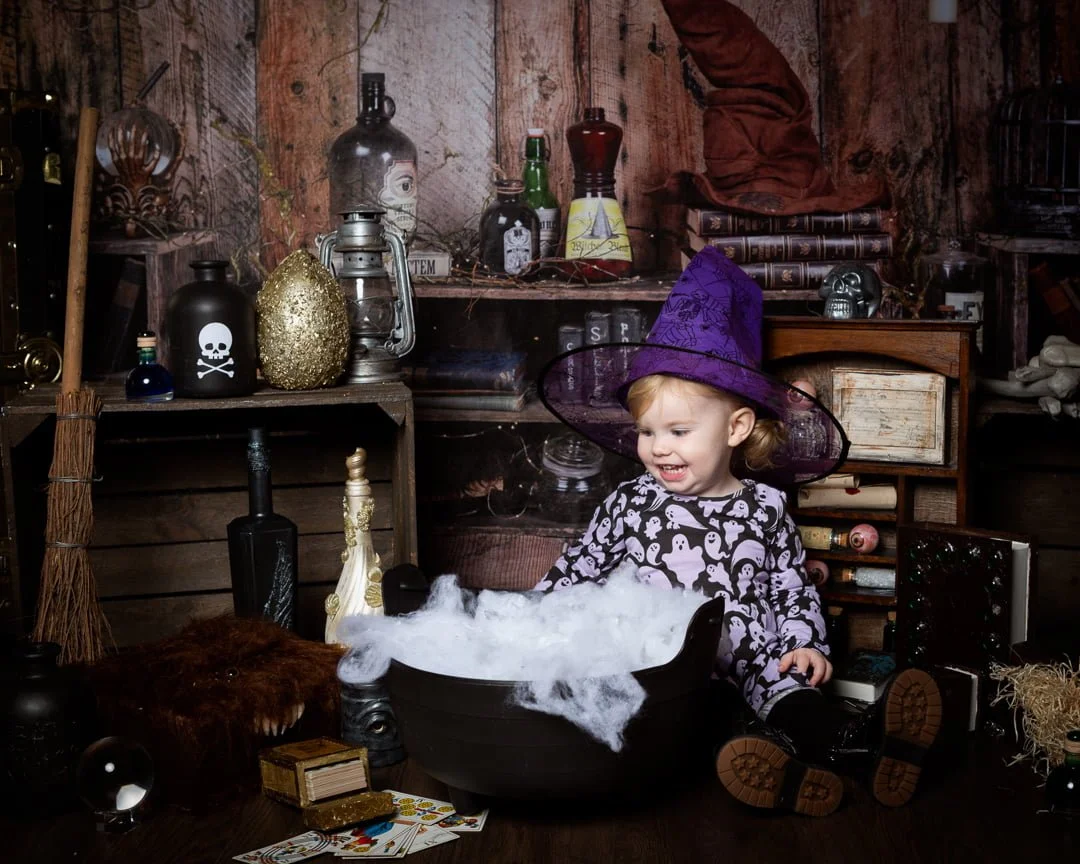 a little witch poses with her cauldron at a halloween themed photo shoot