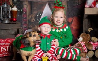 a boy, a girl and a dog all wear matching elf costumes at a christmas photo shoot