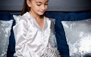 a little girl in christmas pjs sits on a bed at a christmas photo shoot