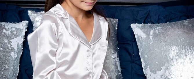 a little girl in christmas pjs sits on a bed at a christmas photo shoot