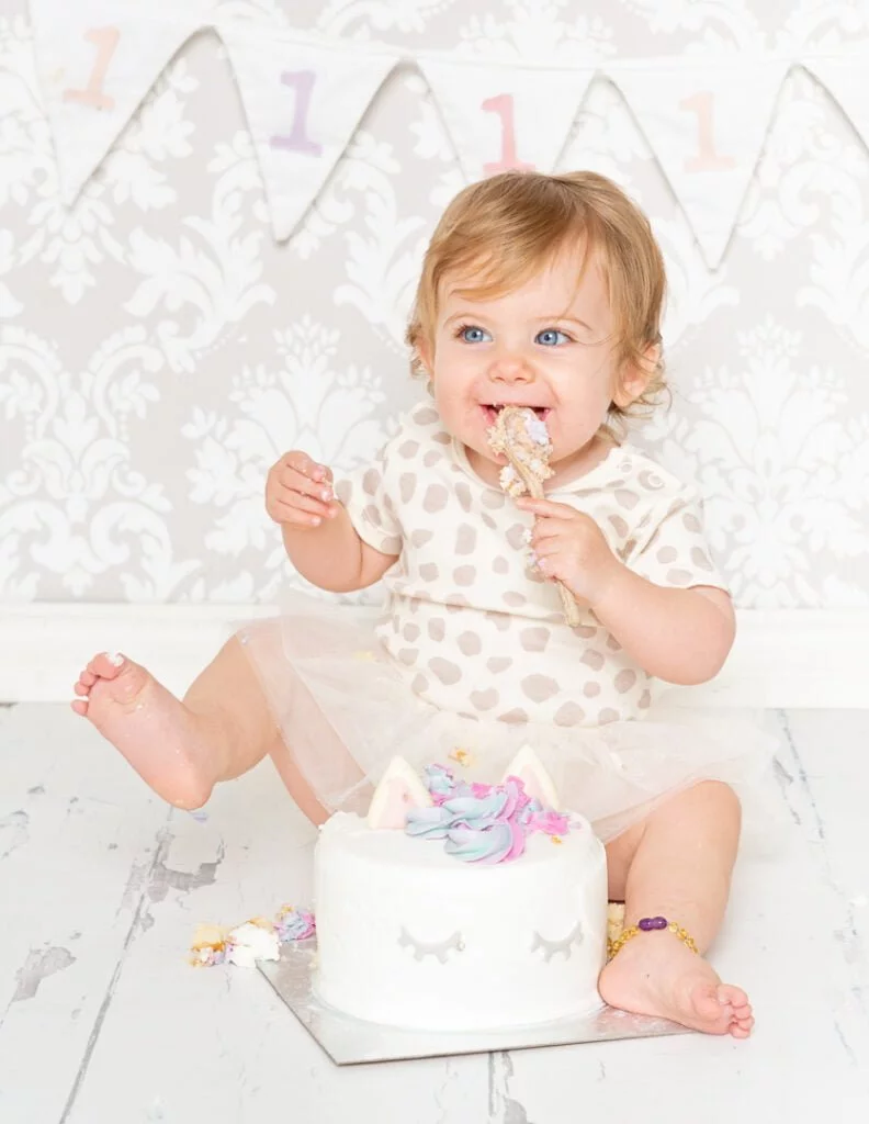 Cake Smash Photo Shoots in East Grinstead West Sussex a little girl enjoys a unicorn themed cake at her first birthday photo shoot