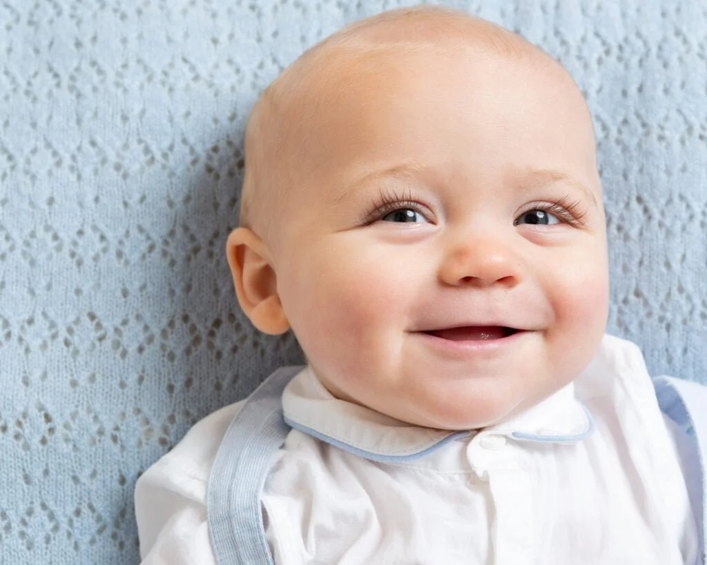 Baby Photography in East Grinstead West Sussex a baby lies on a blue blanket in a matching outfit and smiles up at the camera