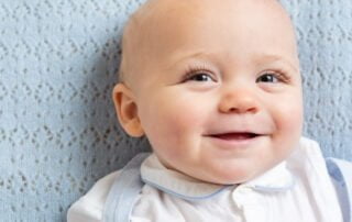a baby lies on a blue blanket in a matching outfit and smiles up at the camera