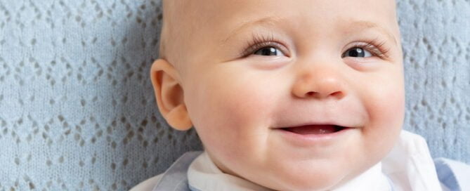a baby lies on a blue blanket in a matching outfit and smiles up at the camera