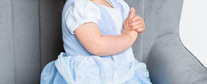a little girl in a princess outfit smiles on a grey chair