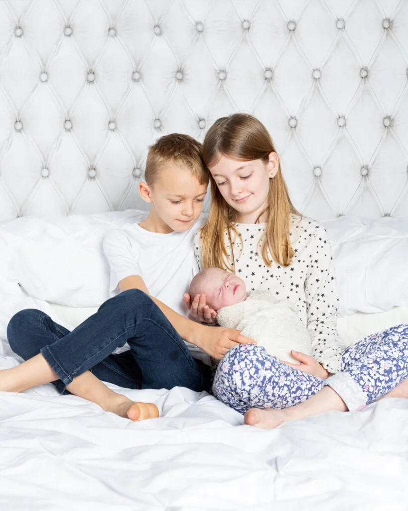 two older siblings hold their newborn sibling on a bed