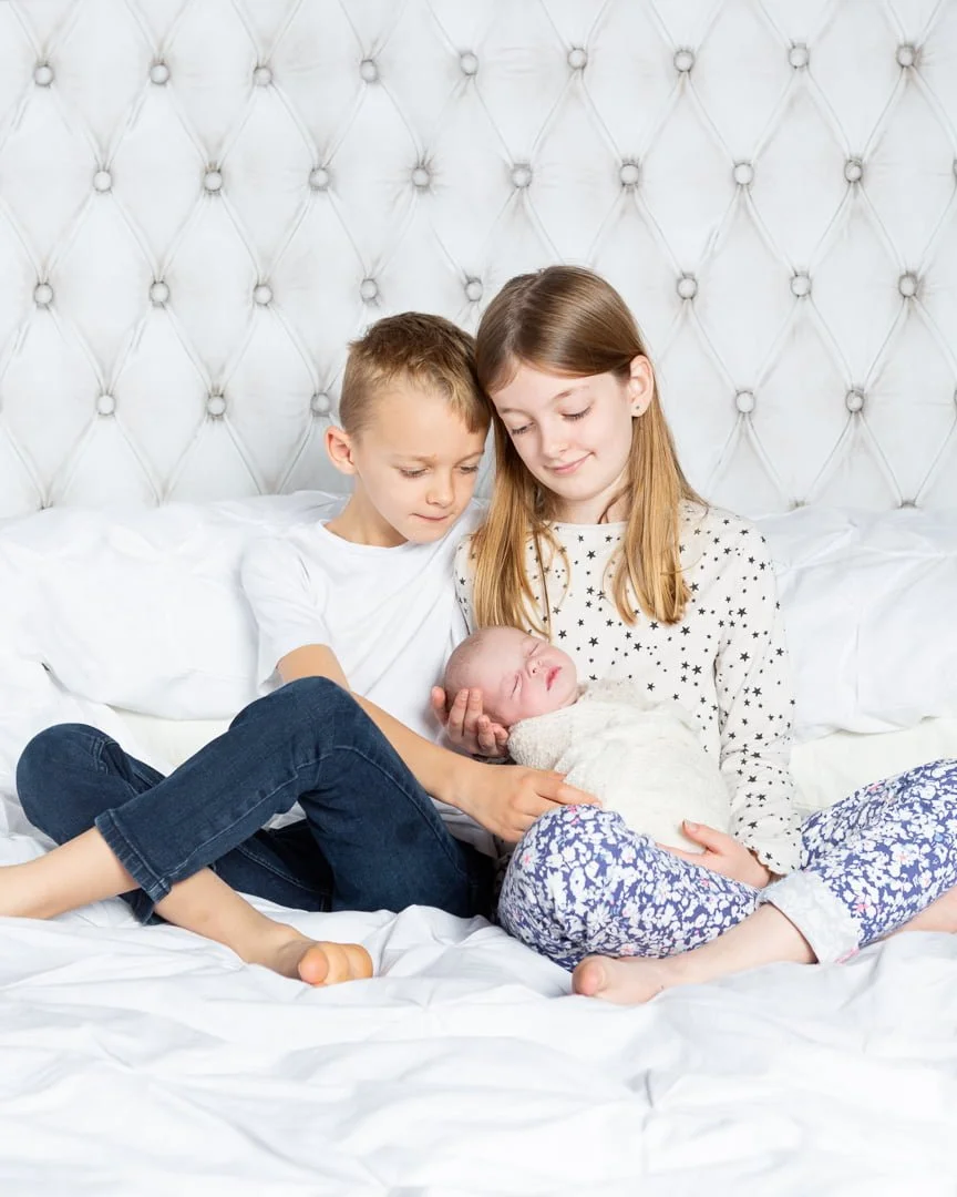 two older siblings hold their newborn sibling on a bed