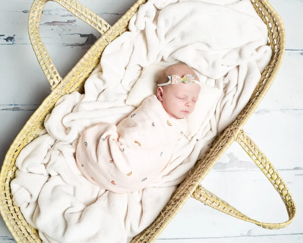 Newborn Photography East Grinstead West Sussex a sleeping newborn wrapped in a blanket and sleeping in a Moses Basket