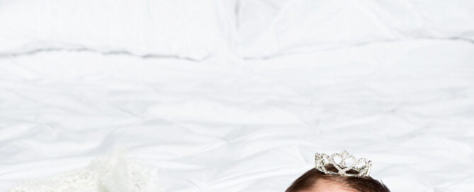 a newborn sleeps on her tummy wearing a sparkly crown