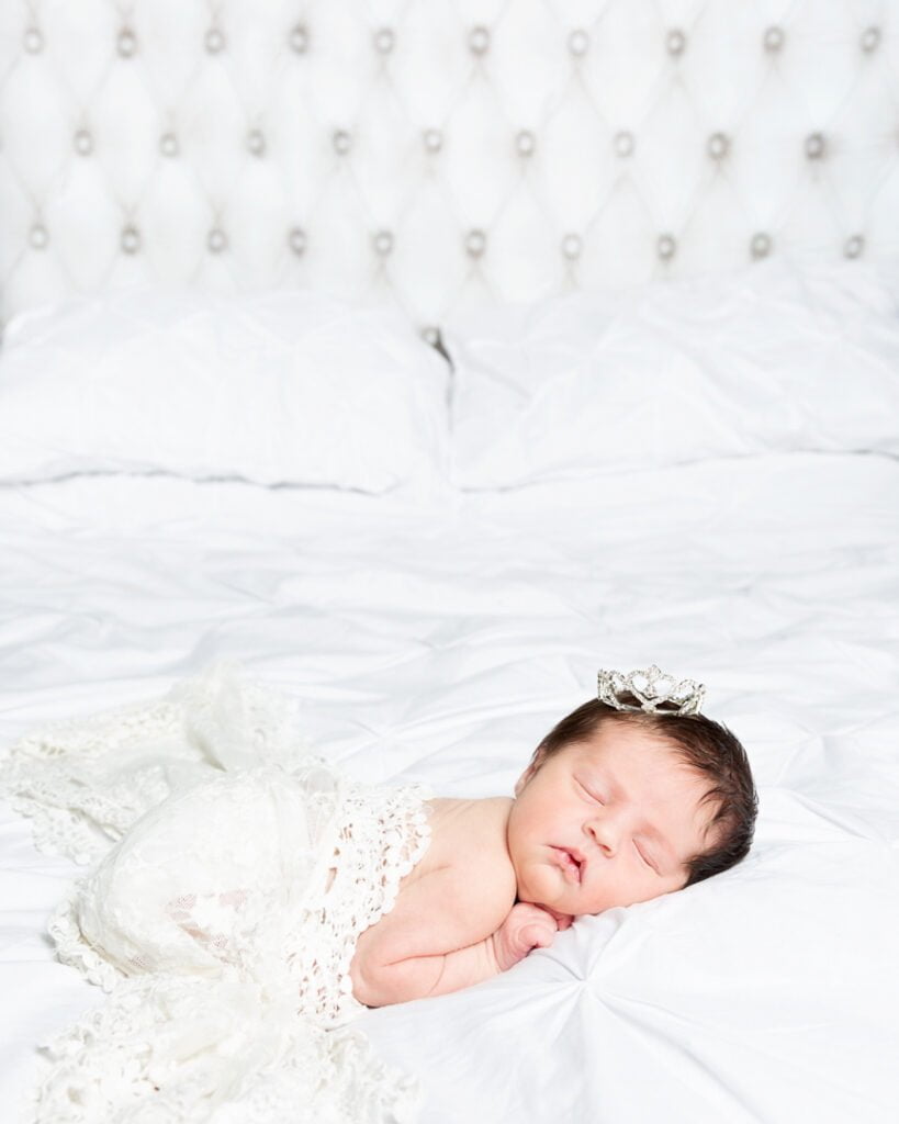 a newborn sleeps on her tummy wearing a sparkly crown