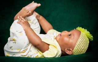 a little girl dressed in yellow plays with her feet while lying on her back