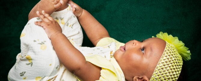 a little girl dressed in yellow plays with her feet while lying on her back