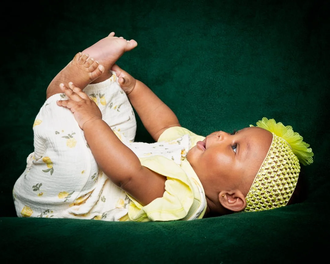 a little girl dressed in yellow plays with her feet while lying on her back