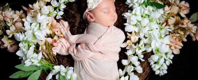 a little girl sleeps in a nest of peach and white flowers