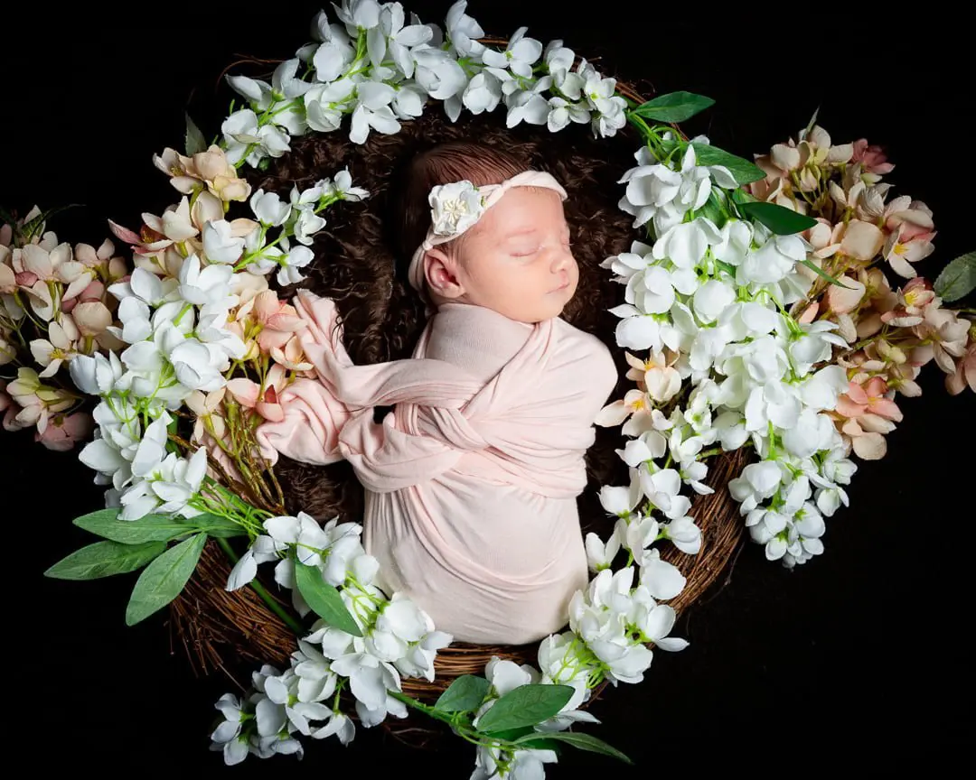 a little girl sleeps in a nest of peach and white flowers