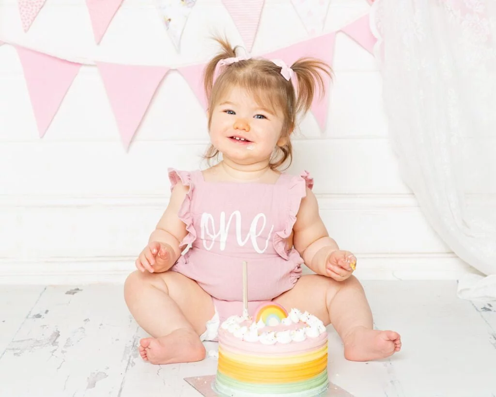 Cake Smash Photography East Grinstead West Sussex a little girl with bunches sits with her birthday cake at a cake smash photo shoot