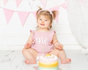 a little girl with bunches sits behind a pastel cake at her cake smash photo shoot