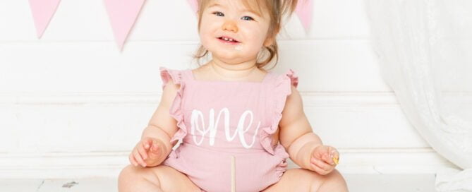 a little girl with bunches sits behind a pastel cake at her cake smash photo shoot