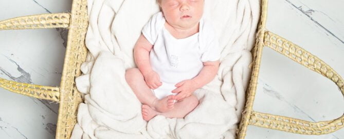 a baby in a white vest sleeping in a Moses basket a photo shoot