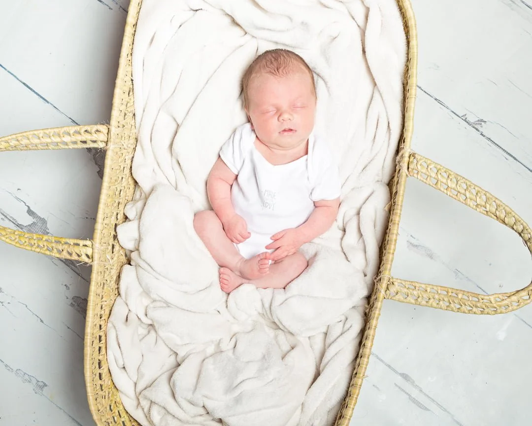 a baby in a white vest sleeping in a Moses basket a photo shoot