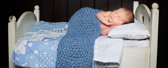 a newborn sleepingon a little white wooden bed with a blue blanket