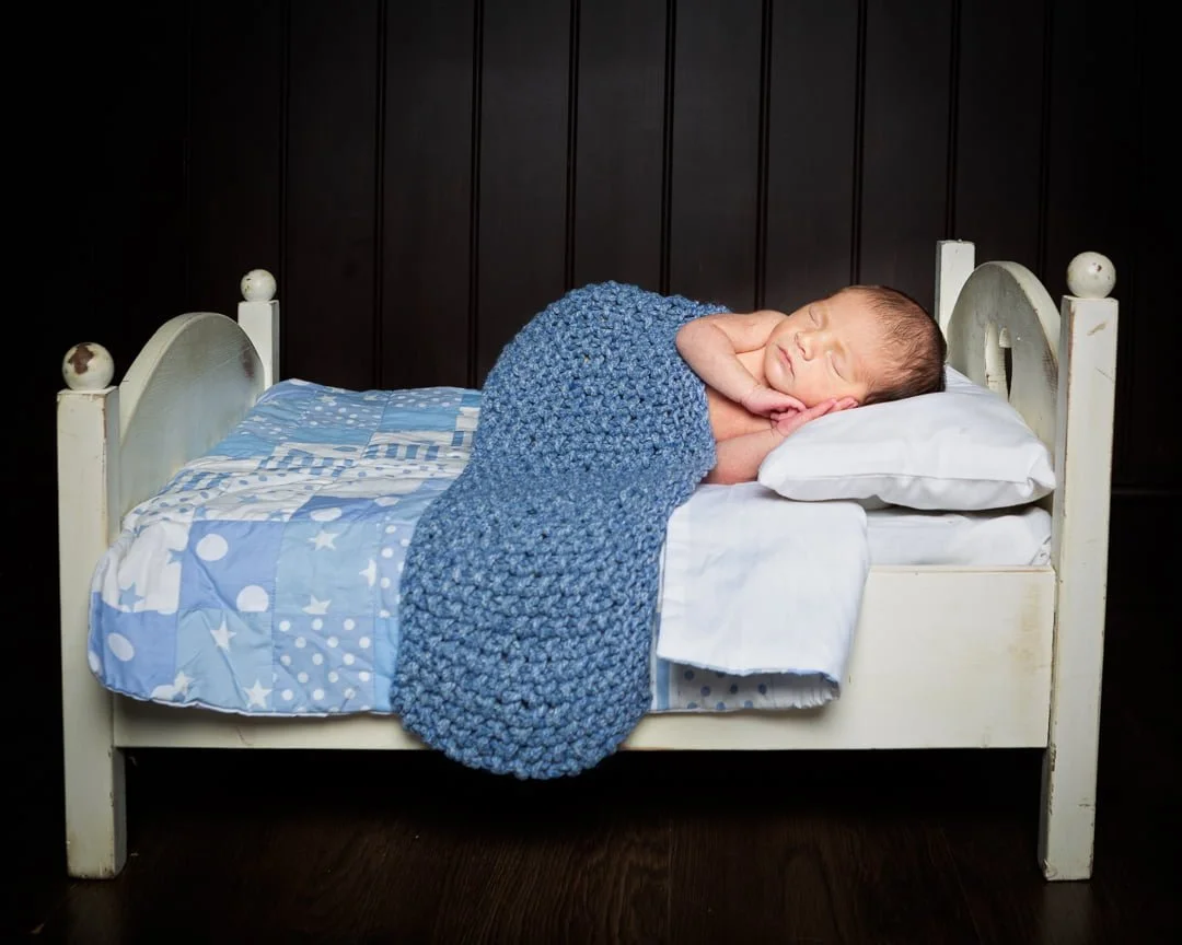 a newborn sleepingon a little white wooden bed with a blue blanket