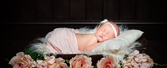 a newborn baby asleep on a dark wood bowls wrapped in peach with peach roses