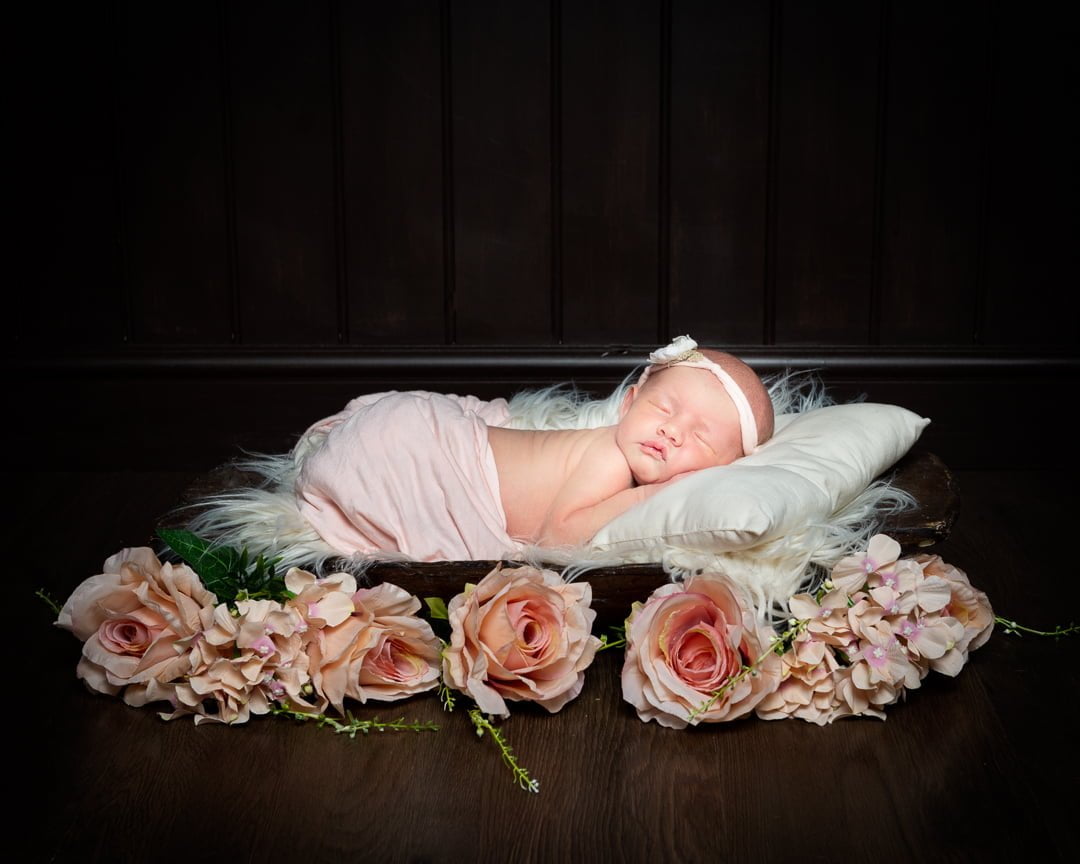 a newborn baby asleep on a dark wood bowls wrapped in peach with peach roses