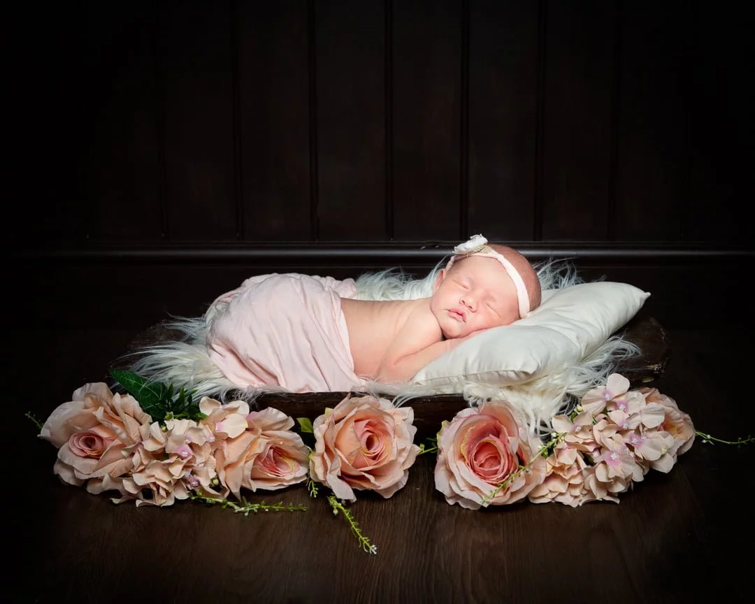 a newborn baby asleep on a dark wood bowls wrapped in peach with peach roses
