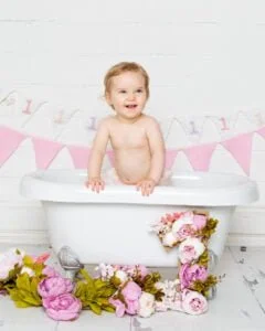 a little girl stands up in the bathtub at her first birthday photo shoot