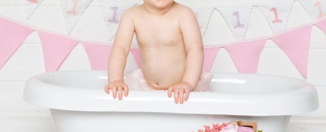 a little girl stands up in the bathtub at her first birthday photo shoot