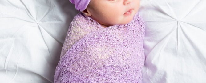 a newborn wrapped in a lilac swaddle
