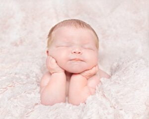 a digitally composited image of a sleeping newborn with their head in their hands