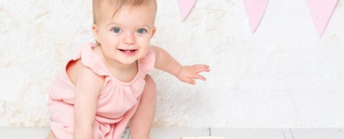 A baby in a superhero landing pose by a cake a professional photo shoot