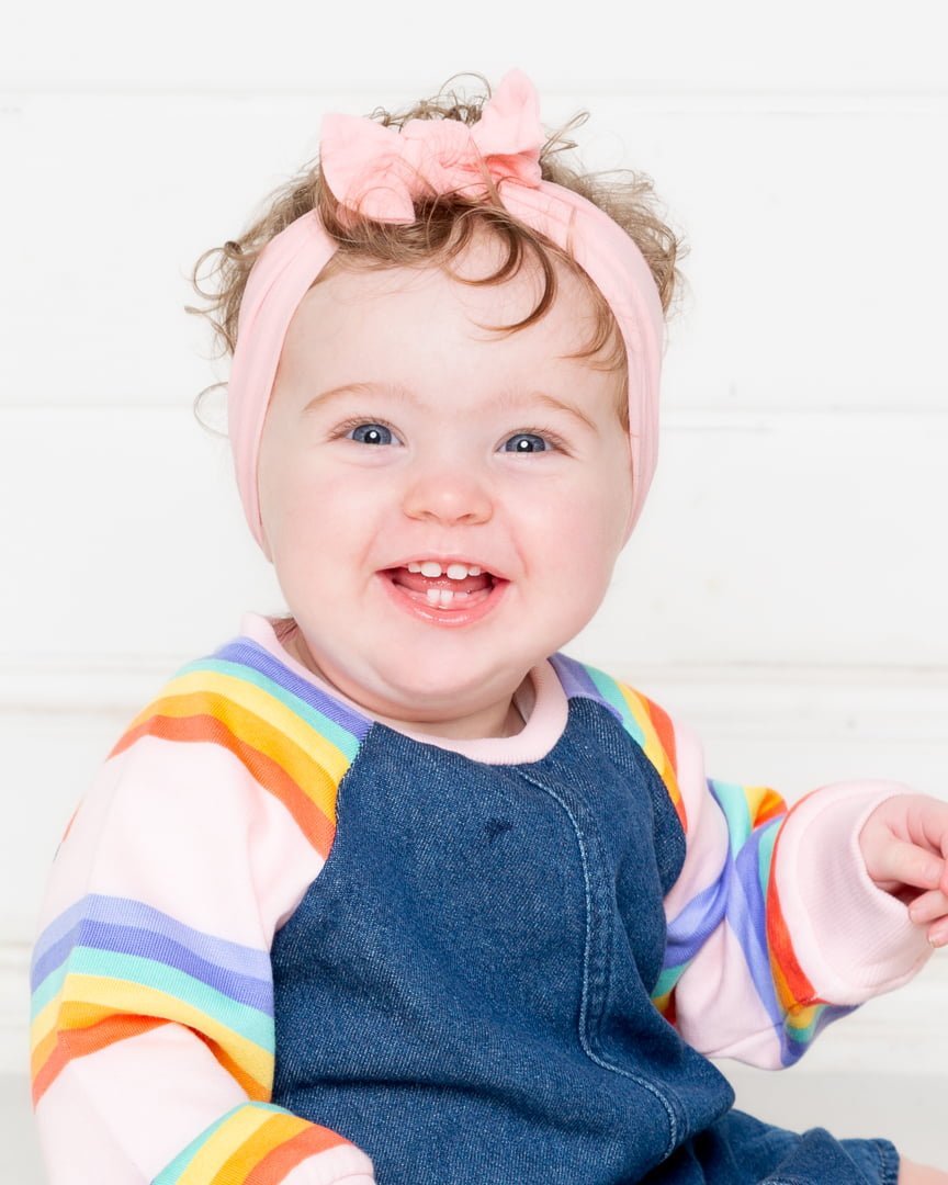 A baby in a denim and rainbow outfit with spots on their face