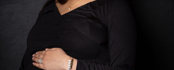 a pregnant woman looks down at her bump in a long black dress
