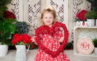 a little girl holds a heart made of roses at a mother's day photo shoot