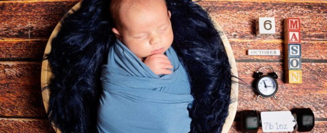 a newborn with a birth announcement prop set in a bowl wrapped in blue
