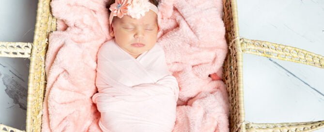a peach blanket in a moses basket with a sleeping wrapped newborn