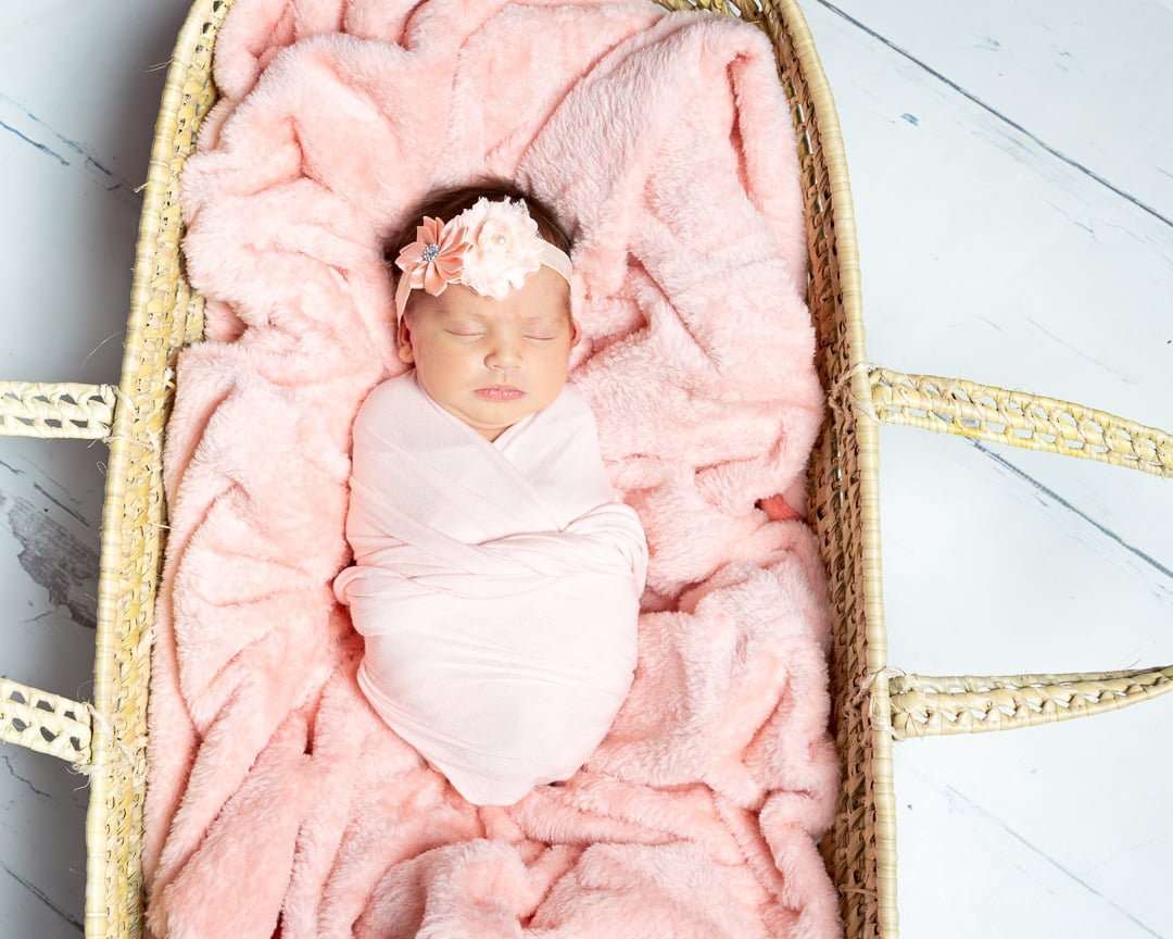 a peach blanket in a moses basket with a sleeping wrapped newborn