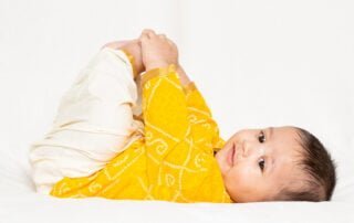 a little baby in happy baby pose in a yellow top