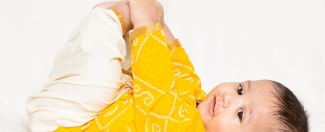 a little baby in happy baby pose in a yellow top